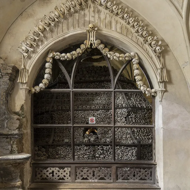 A grated alcove of stacked bones set into a Gothic arch inside the Sedlec Ossuary